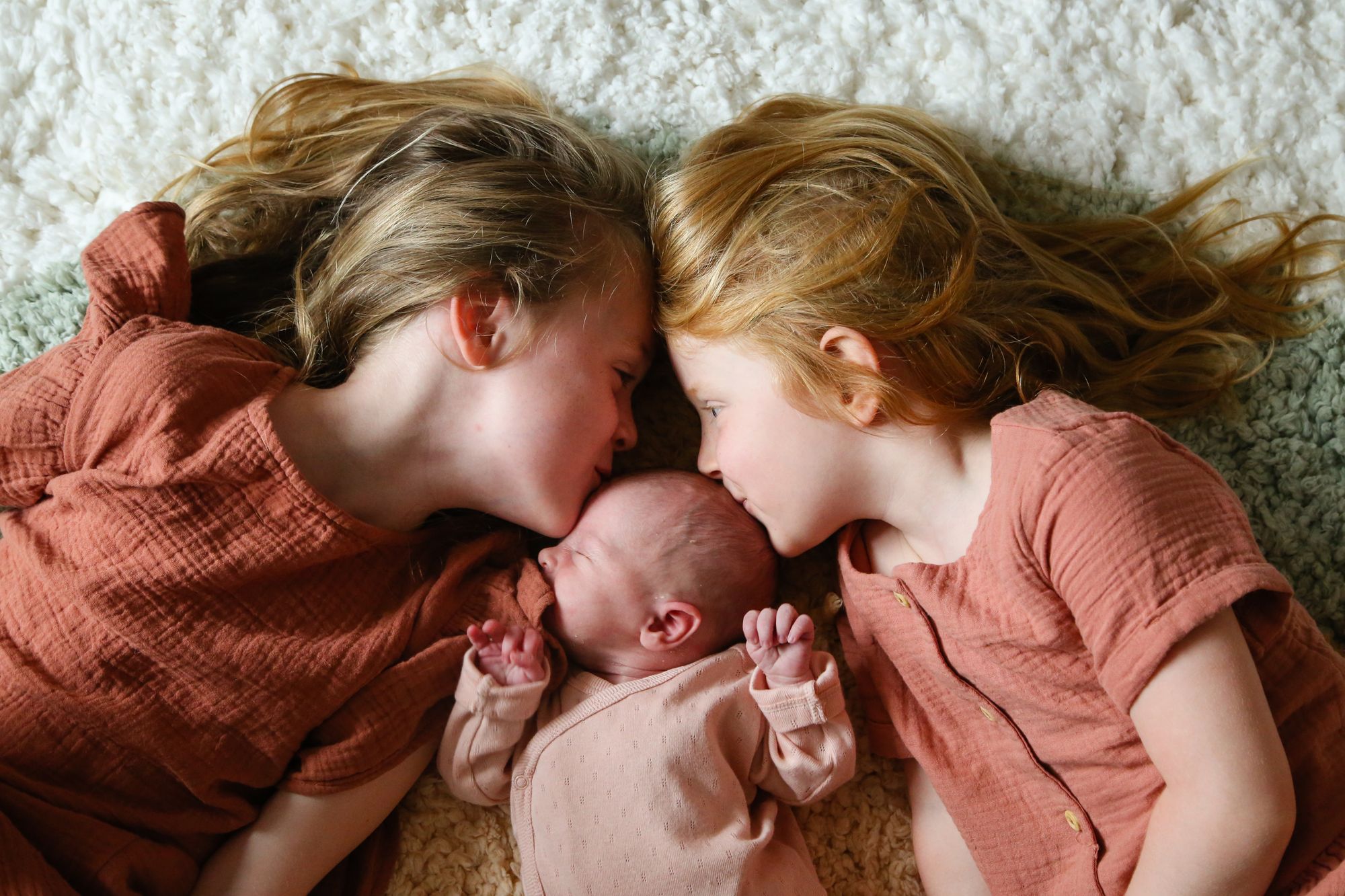 Two sisters kissing newborn baby girl at a home photo shoot by Tanya Aldcroft Photography