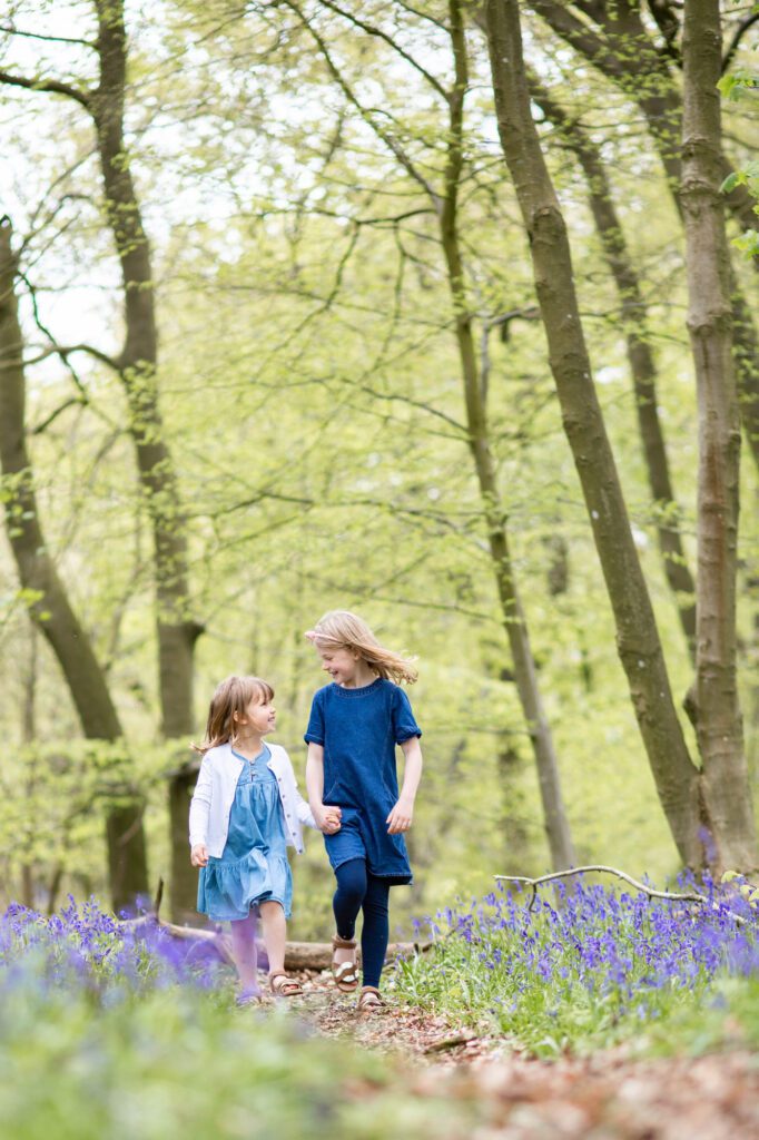 Sisters walking and smiling at bluebell photo shoot near Tring, Hertfordshire by Aldcroft Photography